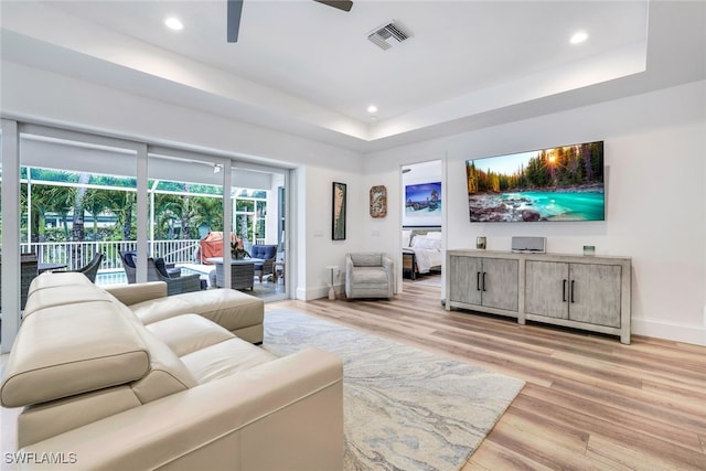 living room featuring ceiling fan, light hardwood / wood-style flooring, and a tray ceiling