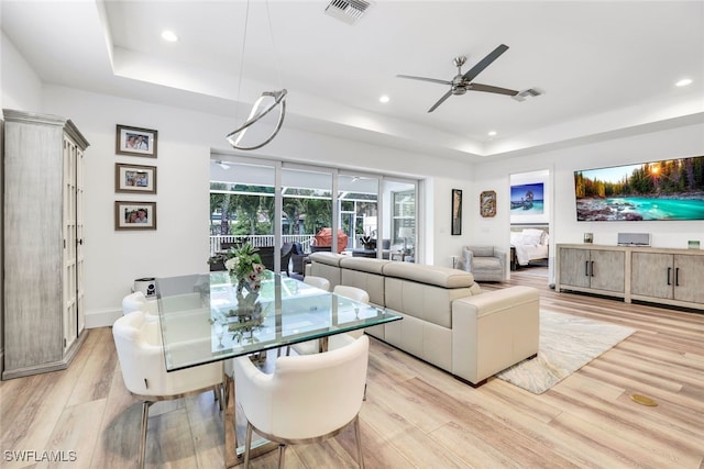 living room with a raised ceiling, ceiling fan, and light hardwood / wood-style flooring