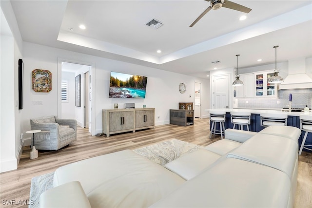 living room with light wood-type flooring, a raised ceiling, and ceiling fan