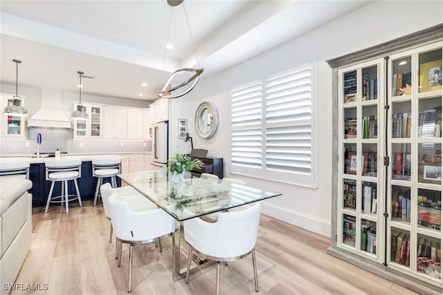 dining room with light wood-type flooring, sink, and a tray ceiling