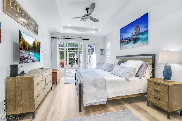 bedroom featuring ceiling fan, french doors, light wood-type flooring, a tray ceiling, and access to outside