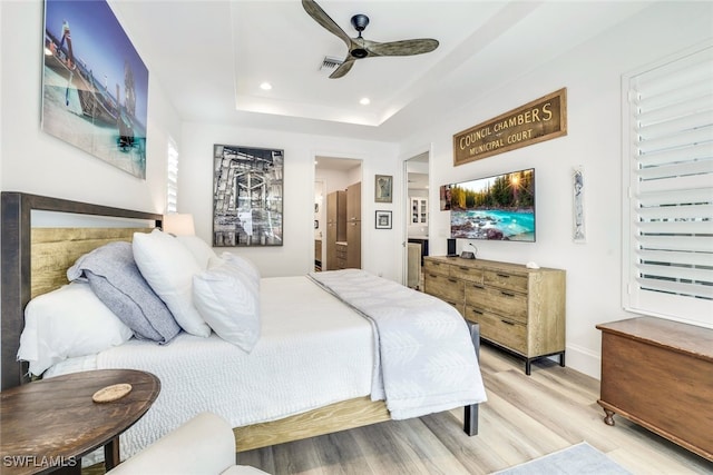 bedroom featuring connected bathroom, hardwood / wood-style flooring, a raised ceiling, and ceiling fan