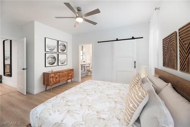 bedroom featuring ceiling fan, a barn door, light hardwood / wood-style floors, and ensuite bath