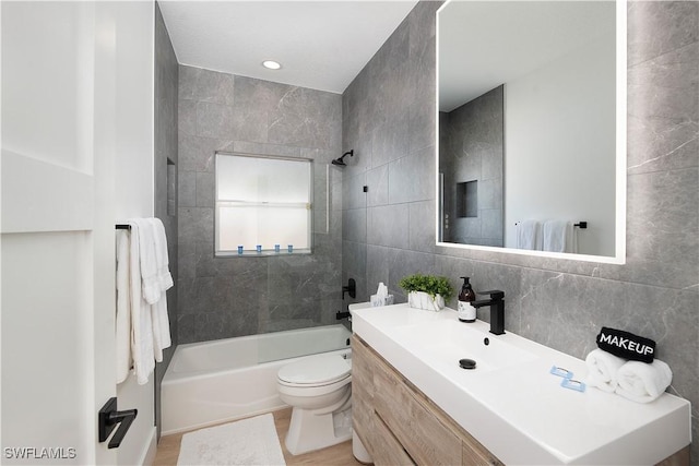 full bathroom featuring backsplash, vanity, tiled shower / bath combo, tile walls, and toilet