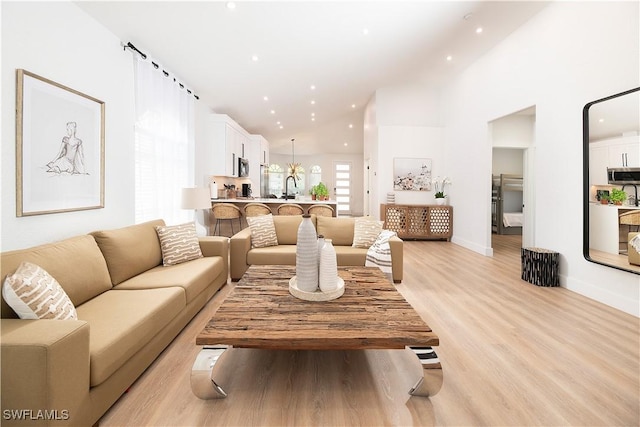 living room with light hardwood / wood-style floors, high vaulted ceiling, and sink