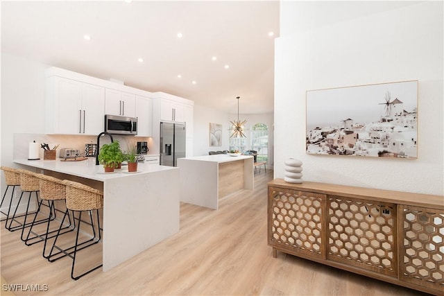 kitchen with a center island, pendant lighting, a breakfast bar, white cabinets, and appliances with stainless steel finishes