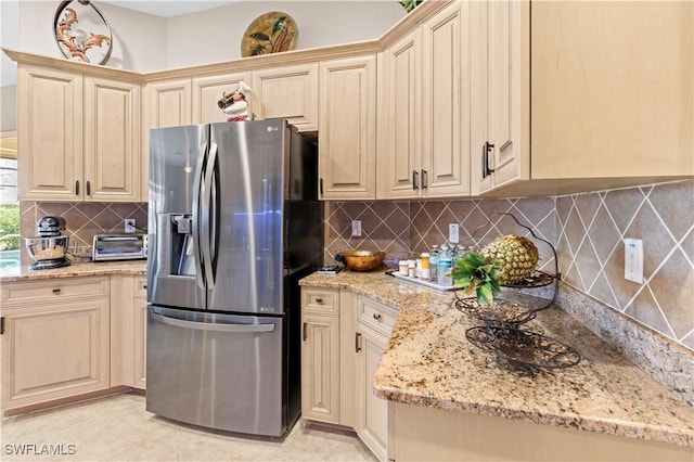 kitchen featuring light tile patterned floors, backsplash, stainless steel fridge with ice dispenser, and light stone counters