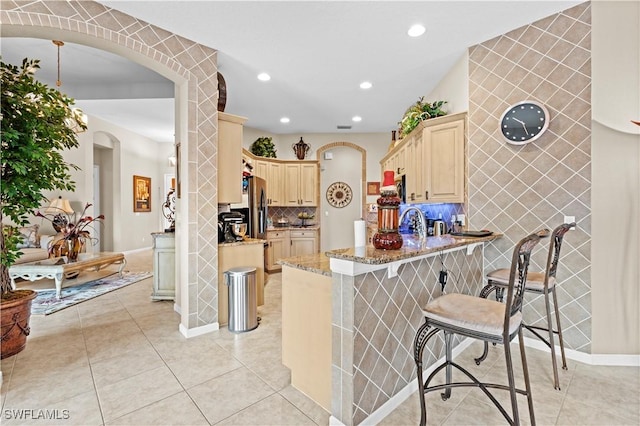 kitchen with backsplash, a breakfast bar, light tile patterned floors, light brown cabinetry, and light stone counters