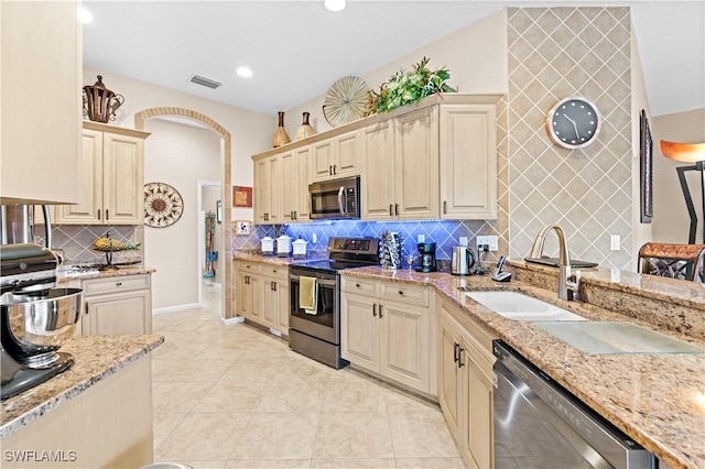 kitchen with backsplash, sink, light stone countertops, appliances with stainless steel finishes, and light tile patterned floors