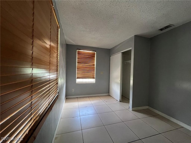 unfurnished bedroom featuring a closet, light tile patterned flooring, and a textured ceiling