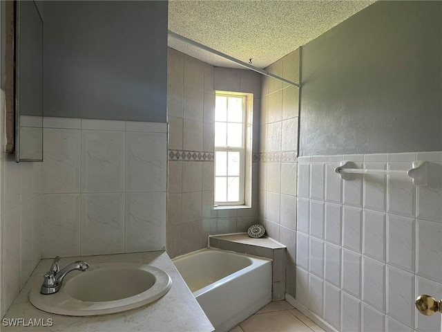 bathroom with a textured ceiling, tile walls, tile patterned floors, and sink