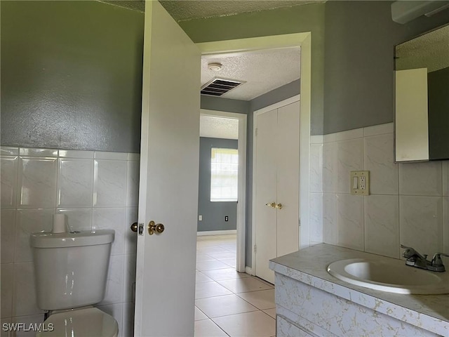 bathroom with toilet, vanity, tile patterned flooring, tile walls, and a textured ceiling