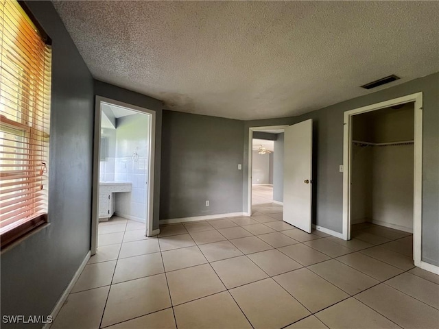 unfurnished bedroom with ensuite bathroom, light tile patterned floors, a closet, and a textured ceiling