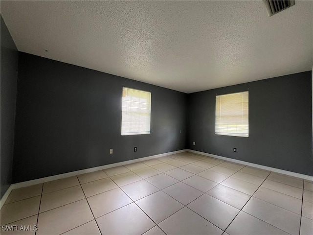 tiled spare room featuring a textured ceiling and a healthy amount of sunlight