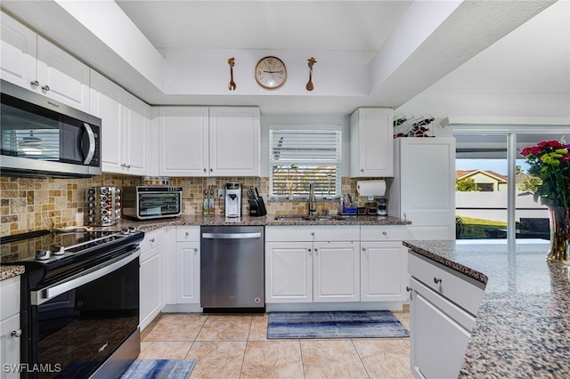 kitchen with appliances with stainless steel finishes, white cabinetry, dark stone countertops, and sink