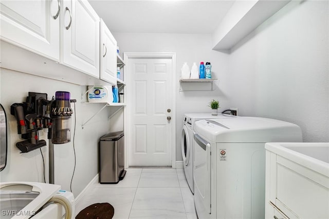 clothes washing area featuring cabinets, light tile patterned floors, and washing machine and dryer