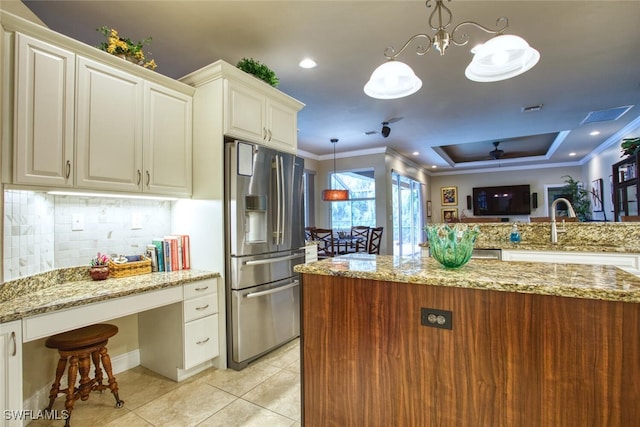 kitchen with ceiling fan with notable chandelier, pendant lighting, backsplash, stainless steel fridge, and a tray ceiling