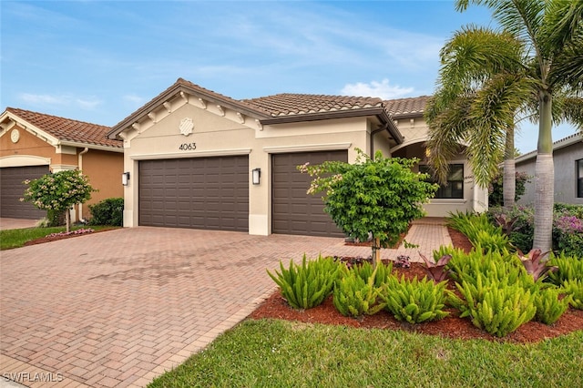 mediterranean / spanish home with a garage, a tiled roof, decorative driveway, and stucco siding