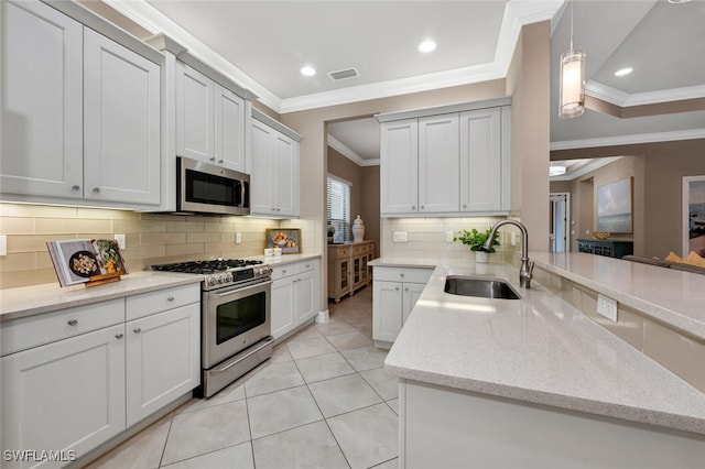 kitchen featuring appliances with stainless steel finishes, white cabinetry, a sink, and decorative light fixtures