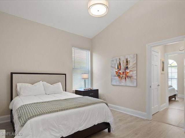 bedroom with baseboards, vaulted ceiling, and light wood finished floors