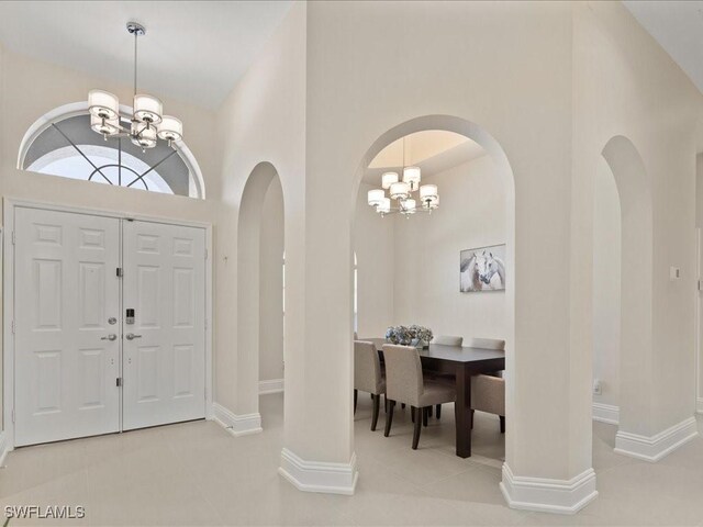 tiled entrance foyer with arched walkways, baseboards, a high ceiling, and an inviting chandelier