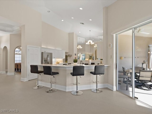 kitchen with a breakfast bar, white cabinetry, stainless steel fridge, light countertops, and a towering ceiling