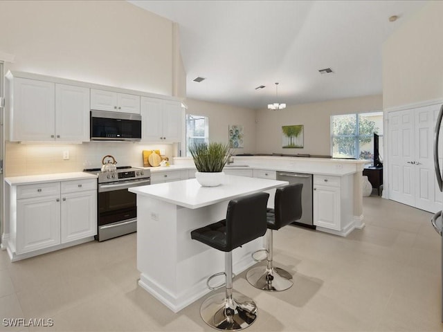 kitchen featuring a center island, light countertops, appliances with stainless steel finishes, white cabinets, and plenty of natural light