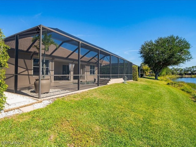 back of house featuring a water view, glass enclosure, a patio, and a yard