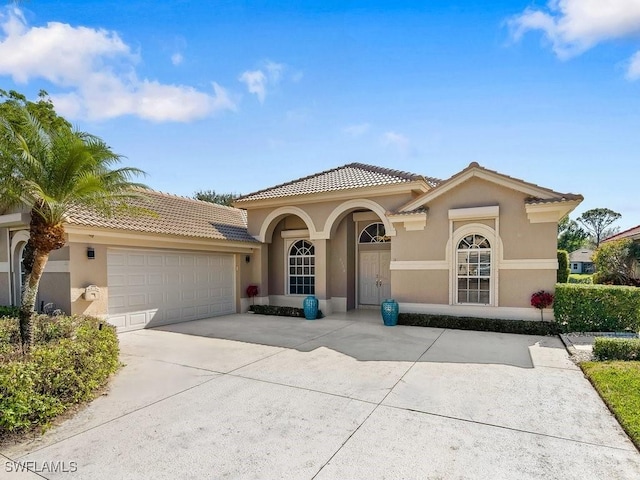 mediterranean / spanish-style house with driveway, an attached garage, a tile roof, and stucco siding