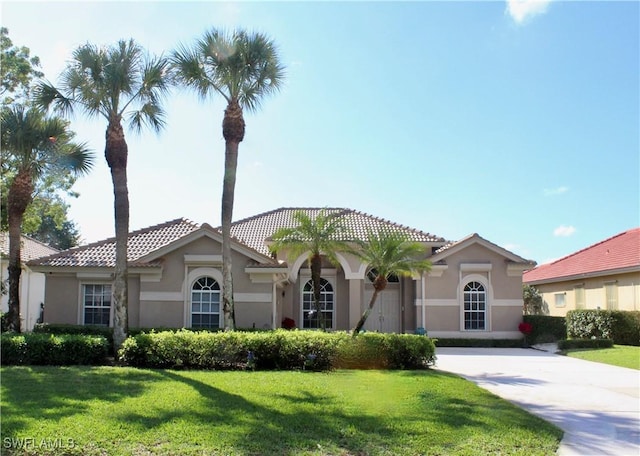 mediterranean / spanish-style home featuring driveway, a front yard, a tile roof, and stucco siding