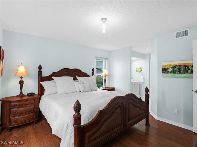 bedroom with ensuite bathroom, dark wood-type flooring, and a textured ceiling