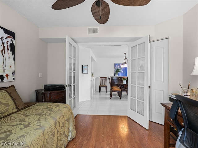 bedroom featuring wood-type flooring, ceiling fan with notable chandelier, and french doors