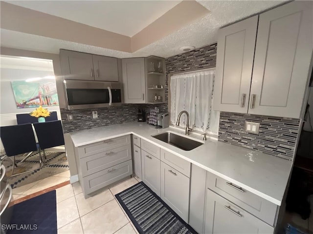 kitchen with sink, light tile patterned floors, gray cabinets, backsplash, and a textured ceiling