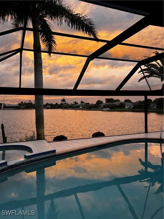 pool at dusk with glass enclosure, a water view, and a hot tub