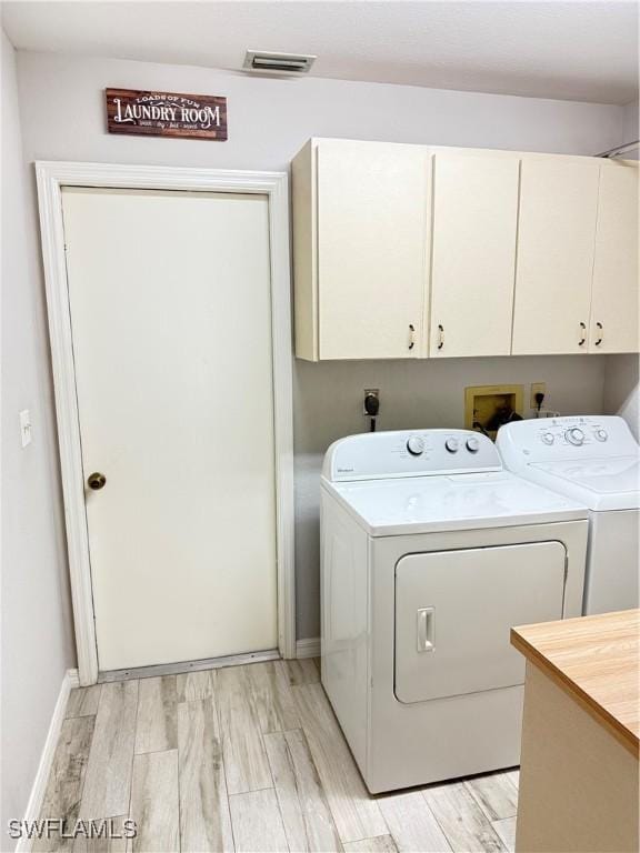 laundry area featuring washing machine and dryer, cabinets, and light wood-type flooring