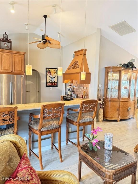 kitchen with stainless steel fridge, a breakfast bar, ceiling fan, hanging light fixtures, and lofted ceiling