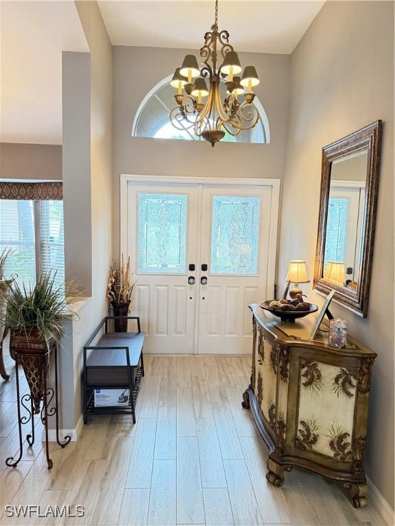 foyer featuring a chandelier, a towering ceiling, light wood-type flooring, and plenty of natural light