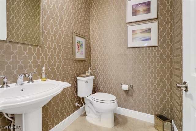 bathroom with tile patterned floors, toilet, a sink, baseboards, and wallpapered walls