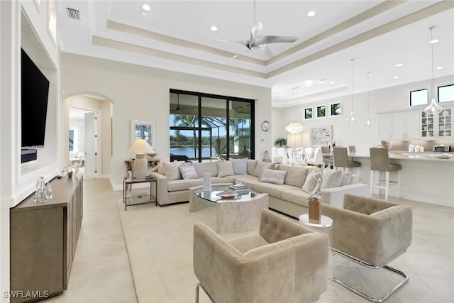 living area with plenty of natural light, visible vents, a raised ceiling, and arched walkways