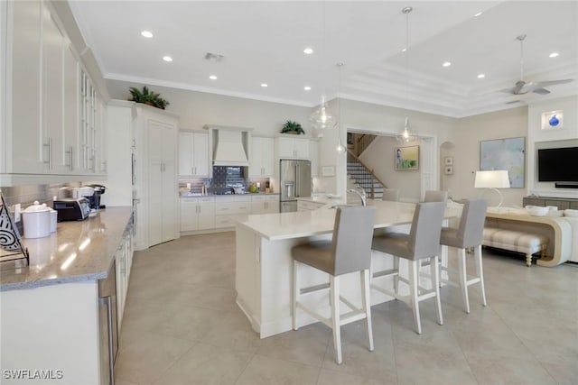 kitchen with a spacious island, white cabinetry, open floor plan, high end fridge, and custom range hood