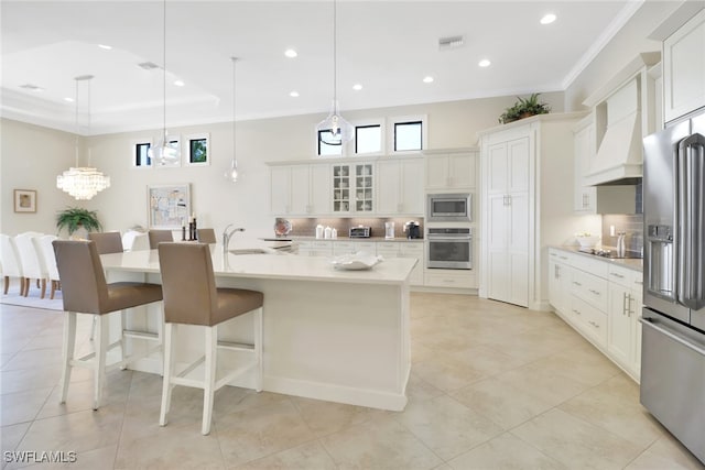 kitchen with white cabinets, glass insert cabinets, appliances with stainless steel finishes, a large island with sink, and pendant lighting