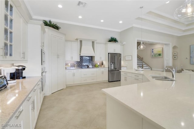 kitchen with appliances with stainless steel finishes, white cabinets, decorative light fixtures, and custom exhaust hood