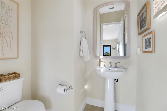 half bathroom featuring toilet, baseboards, and a sink