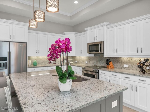 kitchen featuring decorative light fixtures, backsplash, high end appliances, white cabinetry, and a breakfast bar area