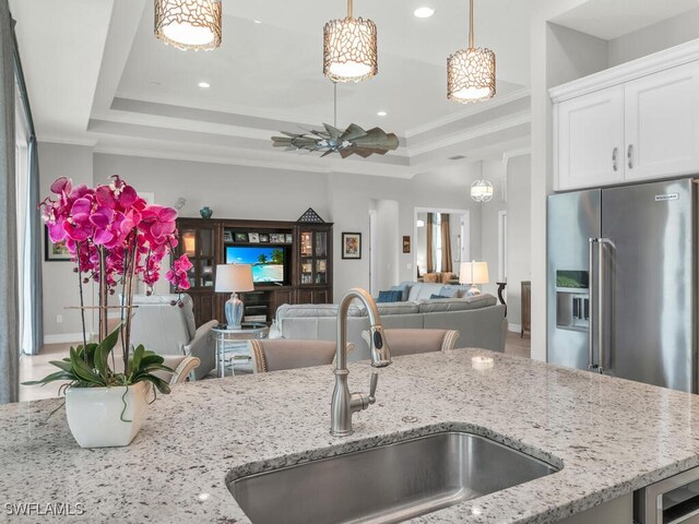 kitchen with light stone countertops, sink, ornamental molding, and a raised ceiling