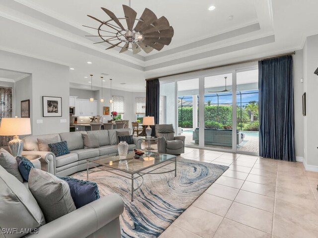 living room featuring light tile patterned floors, ceiling fan, ornamental molding, and a raised ceiling