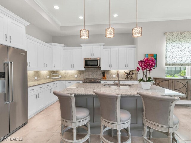 kitchen featuring white cabinetry, a center island with sink, appliances with stainless steel finishes, hanging light fixtures, and sink