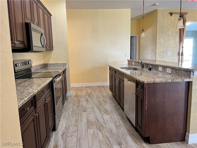 kitchen featuring light stone countertops, dark brown cabinetry, stainless steel appliances, sink, and hanging light fixtures