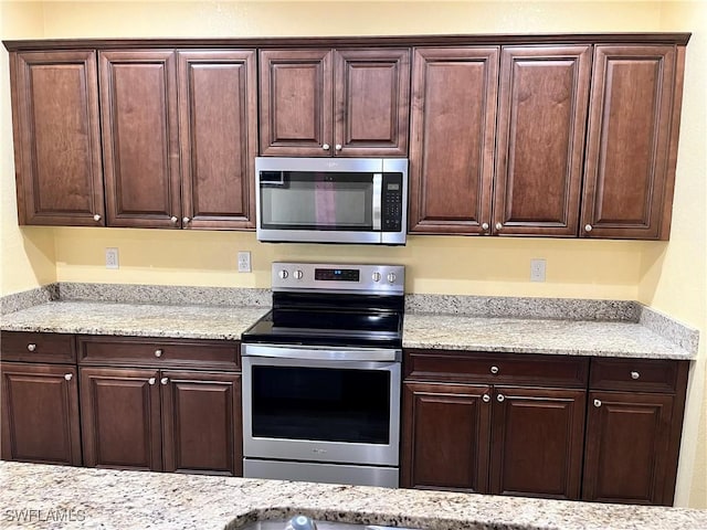 kitchen with dark brown cabinetry, stainless steel appliances, and light stone counters