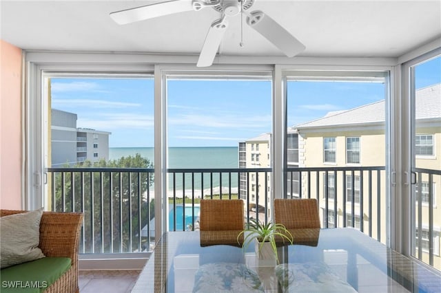 sunroom with ceiling fan and a water view